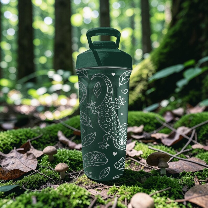 May include: A dark green water bottle with a white lizard and leaf design. The bottle has a handle and a screw-on lid. The design includes a lizard, leaves, hearts, and other shapes. The bottle is cylindrical and appears to be made of metal or plastic.