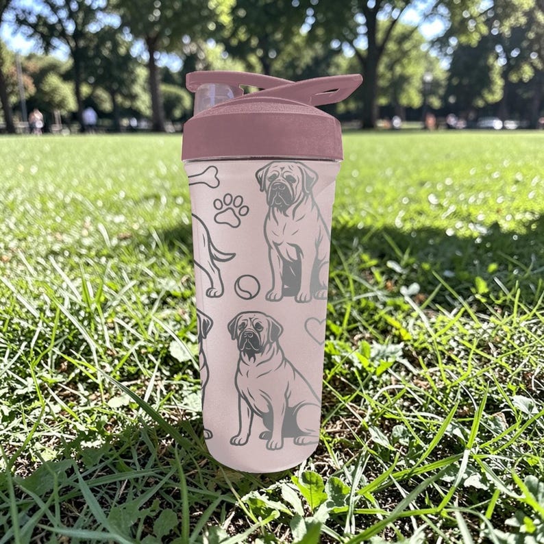 May include: A pink water bottle with a flip-top lid, featuring a repeating pattern of dog illustrations, paw prints, and a bone. The bottle is sitting on green grass.