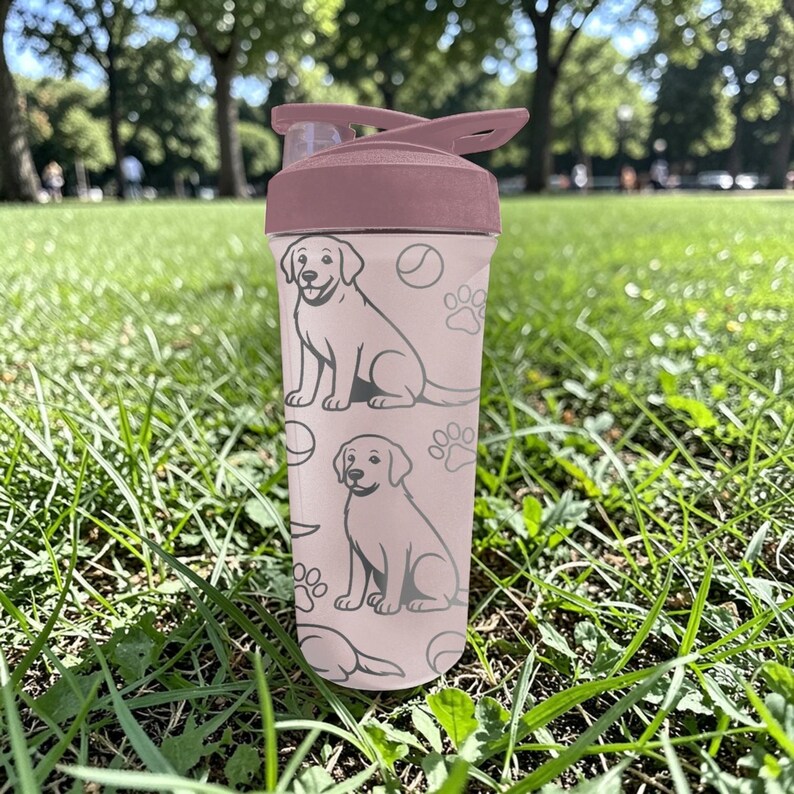 May include: A pink water bottle with a flip-top lid, featuring a repeating pattern of dog illustrations, paw prints, and tennis balls. The bottle is made of clear plastic and is suitable for carrying liquids. The lid is a darker shade of pink.