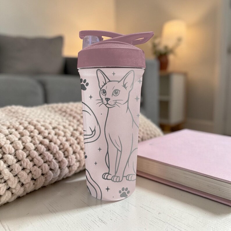 Puede incluir: Una botella de agua rosa con tapa abatible. La botella presenta una ilustraci&oacute;n de gato con huellas de patas y estrellas. La tapa y la parte superior de la botella son de un tono rosa m&aacute;s oscuro. La botella est&aacute; sobre una superficie blanca.