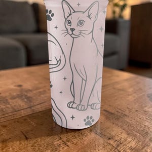 Puede incluir: Un vaso alto de color rosa claro con una ilustraci&oacute;n detallada de un gato, huellas de patas y estrellas. El gato est&aacute; representado en posici&oacute;n sentada con un contorno detallado. El dise&ntilde;o se repite alrededor del vaso.