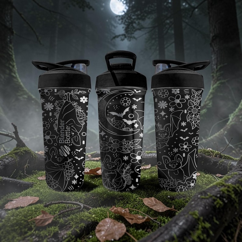 Pu&ograve; includere: Tre bottiglie Blender nere con illustrazioni bianche di pipistrelli, fiori e lune. Ogni bottiglia ha un coperchio e un manico neri. Le bottiglie sono su una superficie muschiosa con uno sfondo di foresta e una luna piena.