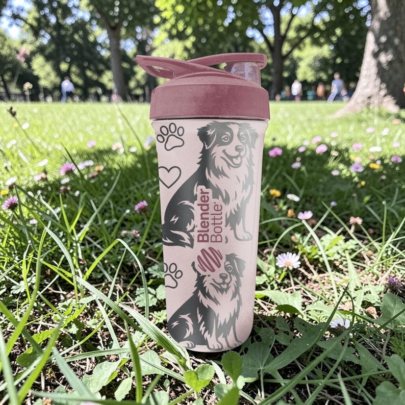 K&ouml;nnte beinhalten: Eine rosa Blender Bottle mit einem weinroten Deckel und einem Hunde-Motiv. Die Flasche hat Pfotenabdr&uuml;cke, ein Herz und die Worte "Blender Bottle". Die Flasche ist zylindrisch und aus Kunststoff.