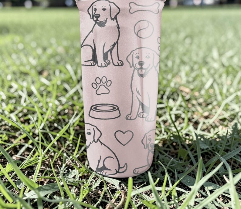 May include: A pink tumbler decorated with black line drawings of Labrador Retrievers, paw prints, a dog bowl, a bone, a ball, and hearts. The tumbler is cylindrical and appears to be made of metal or plastic.