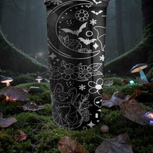 Pu&ograve; includere: Bicchiere nero con un'illustrazione bianca di pipistrelli, fiori e una luna crescente. Il design include un pipistrello con una corona di fiori. Il bicchiere &egrave; ambientato in una scena di foresta con funghi luminosi.