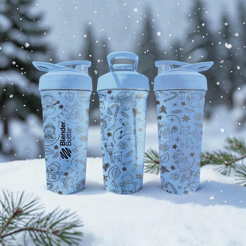Puede incluir: Tres botellas Blender Bottle de color azul claro con ilustraciones de invierno. Cada botella tiene una tapa abatible y un asa. Las botellas est&aacute;n decoradas con copos de nieve, mu&ntilde;ecos de nieve y otros dise&ntilde;os festivos. El logotipo de Blender Bottle es visible.
