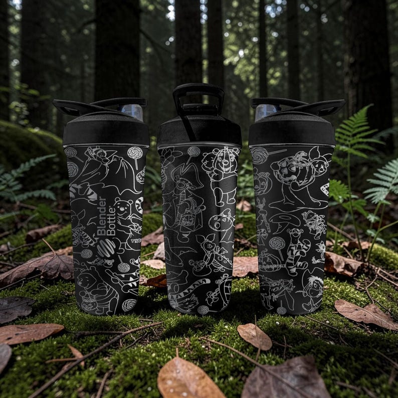 May include: Three black Blender Bottles with white cartoon character designs. The bottles are on moss and leaves in a forest. Each has a black lid with a flip-top opening. The text "Blender Bottle" is visible on one bottle.