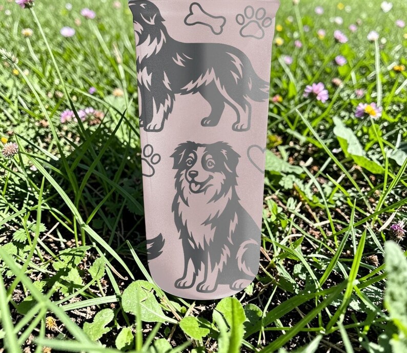 K&ouml;nnte beinhalten: Ein hellrosa Becher mit zwei Hundeillustrationen, Pfotenabdr&uuml;cken, einem Knochen und Herzen. Ein Hund steht, der andere sitzt. Der Becher ist von gr&uuml;nem Gras und kleinen lila Blumen umgeben.