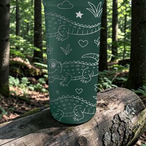 Peut inclure: Un gobelet vert fonc&eacute; avec un motif de crocodiles blancs, de nuages, d'&eacute;toiles et de c&oelig;urs. Le gobelet cylindrique est probablement en m&eacute;tal. Le design est ludique et convient &agrave; tous les &acirc;ges. Il peut contenir environ 470 ml.