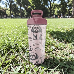May include: A pink water bottle featuring a Shih Tzu dog illustration, paw prints, and dog bone designs. The bottle has a matching pink lid and handle. The background shows a grassy area with trees.
