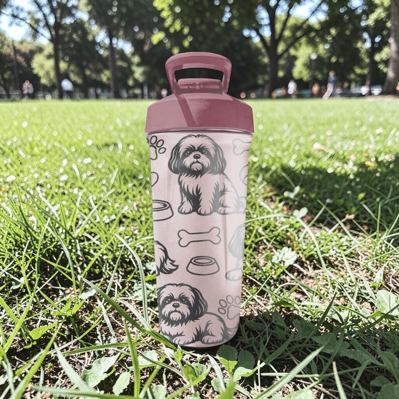 May include: A pink water bottle featuring a Shih Tzu dog illustration, paw prints, and dog bone designs. The bottle has a matching pink lid and handle. The background shows a grassy area with trees.