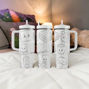 May include: Three white Stanley tumblers with handles and straws, featuring a repeating black line art pattern of bedtime items including a smiling pillow, a folded blanket, an alarm clock, a book, a mug, slippers, a teddy bear, and a sleep mask.