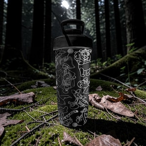 May include: Black water bottle with white cartoon character illustrations. The bottle has a black handle and lid. The background is a forest scene with moss and fallen leaves.