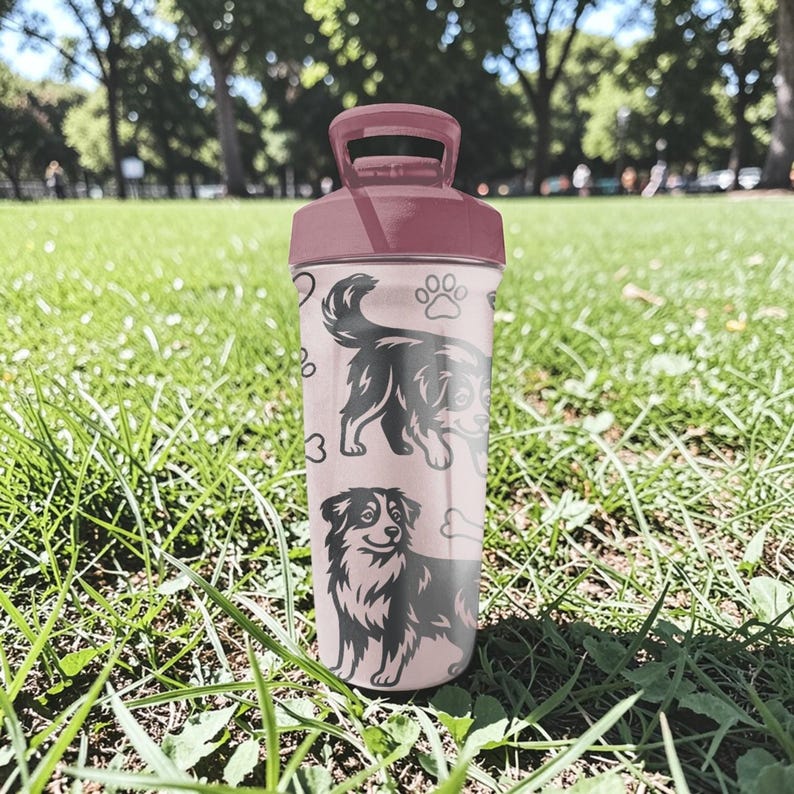 K&ouml;nnte beinhalten: Eine rosa Wasserflasche mit einem weinroten Deckel und Griff. Die Flasche zeigt schwarze Illustrationen von Hunden, Pfotenabdr&uuml;cken und einem Knochen. Der Hintergrund ist eine gr&uuml;ne Wiese mit B&auml;umen.
