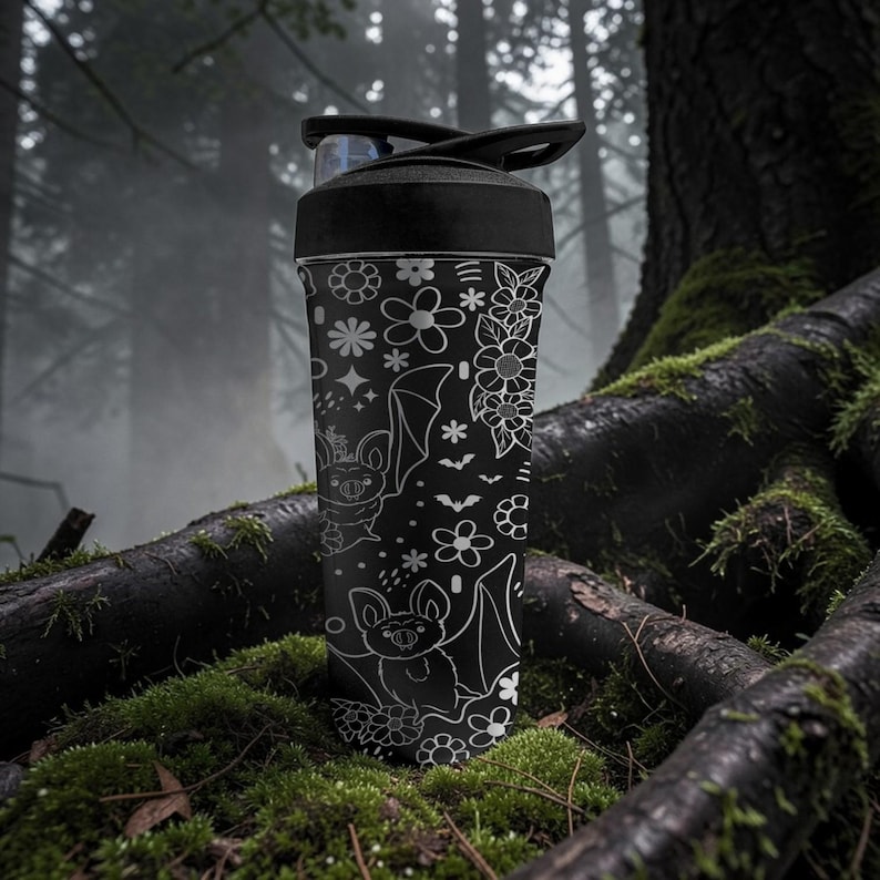 Pu&ograve; includere: Borraccia nera con coperchio nero, con un motivo floreale e di pipistrelli bianco. Il design include vari fiori, stelle e illustrazioni di pipistrelli. La borraccia &egrave; cilindrica e sembra essere in metallo.