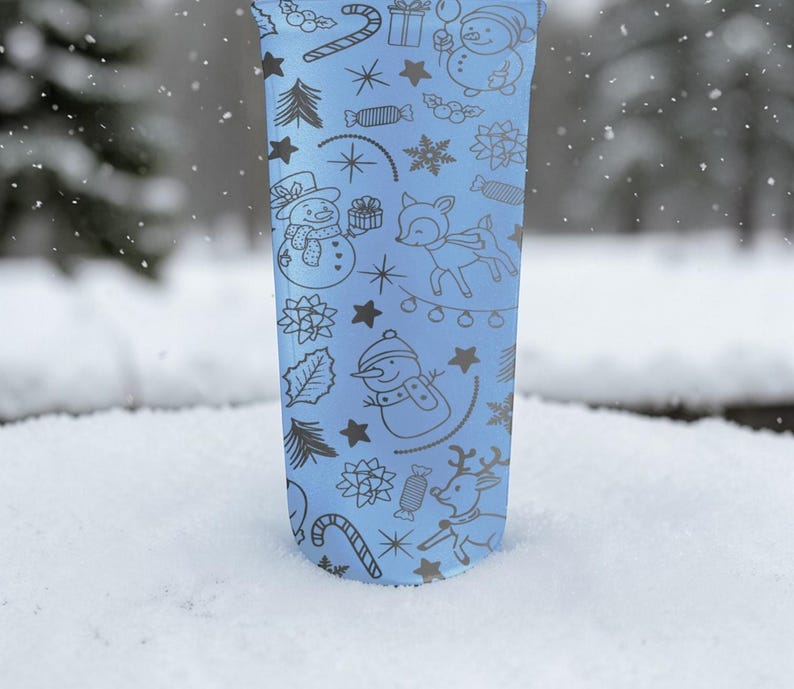 Puede incluir: Un vaso azul claro con un dise&ntilde;o de vacaciones de invierno. El dise&ntilde;o incluye mu&ntilde;ecos de nieve, renos, bastones de caramelo, estrellas y copos de nieve. El vaso est&aacute; en la nieve.
