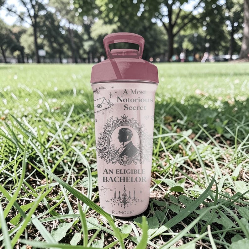 Pode incluir: Uma garrafa de &aacute;gua rosa e gren&aacute; com uma al&ccedil;a. A garrafa apresenta o texto "A Most Notorious Secret" e "An Eligible Bachelor" com a silhueta de um homem em uma moldura decorativa. A palavra "RUMOUR" est&aacute; na parte inferior.