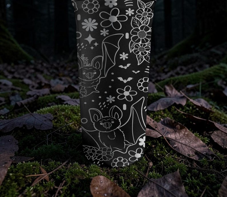 Pu&ograve; includere: Bicchiere nero con un motivo floreale e pipistrelli bianchi. Il design include vari fiori, stelle e illustrazioni di pipistrelli. Il bicchiere cilindrico &egrave; mostrato in posizione verticale su uno sfondo naturale.