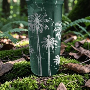 Może przedstawiać: Ciemnozielony kubek z białym wzorem palm. Projekt zawiera kilka palm o r&oacute;żnych rozmiarach na tle białych chmur. Kubek jest cylindryczny i wydaje się być wykonany z metalu.