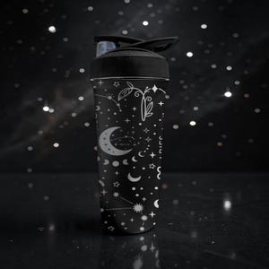Pode incluir: Garrafa de &aacute;gua preta com tampa preta e design celestial. A garrafa apresenta ilustra&ccedil;&otilde;es brancas de luas, estrelas, constela&ccedil;&otilde;es e elementos bot&acirc;nicos. O design est&aacute; em um fundo preto.