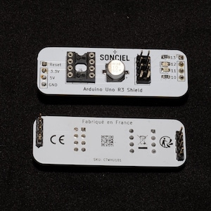 Peut inclure: Deux cartes de circuits imprimés blanches Arduino Uno R3 Shield. La carte supérieure porte l'inscription "SONCIEL" et "Arduino Uno R3 Shield". La carte inférieure porte l'inscription "Fabriqué en France" et "SKU: CTWHU101".