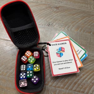 May include: A red and black zippered case holding colourful dice and game cards. The dice are in various colours, including red, green, blue, and purple. The game cards have the text "DICE GAMES" and instructions.