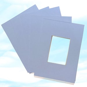 Puede incluir: Varios paspartús de color azul claro con aberturas rectangulares. Los paspartús están apilados, con uno en primer plano y los demás abanicados detrás. Los paspartús están hechos de papel grueso o cartón.