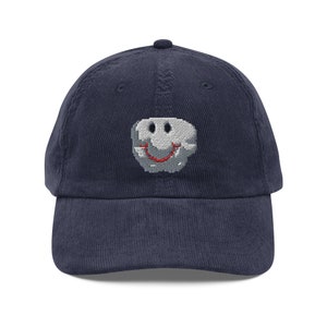 May include: A navy blue corduroy baseball cap with a gray smiley face embroidered on the front.