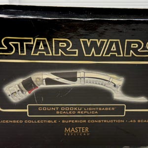Puede incluir: Caja negra con el logo de Star Wars en dorado. Muestra una r&eacute;plica a escala del sable de luz del Conde Dooku. El sable de luz tiene un mango plateado y negro con detalles rojos. La caja indica "Coleccionable con licencia".