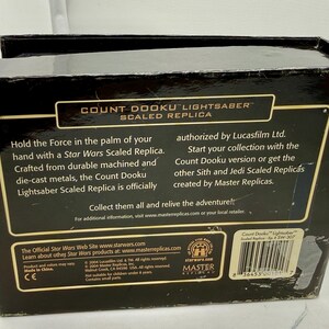 Puede incluir: Una caja negra con el texto "COUNT DOOKU LIGHTSABER SCALED REPLICA" y la marca Star Wars. La caja describe la r&eacute;plica como fabricada con metales mecanizados y fundidos a presi&oacute;n duraderos. La caja tambi&eacute;n incluye un c&oacute;digo de barras y el texto "Made in China."