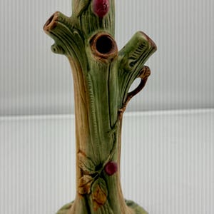May include: A ceramic tree trunk vase with a green and brown finish. The vase features three openings and is decorated with red berries and leaves. The base is round and textured.