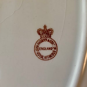 May include: Close-up of a brown stamp on a white ceramic plate. The stamp reads "John Haddock & Son, England, Royal Vitreous".