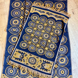 May include: Two rectangular woven rugs featuring a deep blue background with a repeating golden yellow circular medallion pattern. Both rugs have a decorative border with intricate scrollwork and short fringe along the shorter edges.
