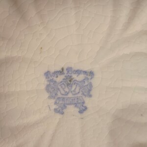 May include: Close-up of a blue and white Royal Bayreuth Bavaria mark on a white ceramic surface.