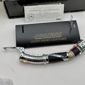 Puede incluir: Una r&eacute;plica del sable de luz del Conde Dooku de Star Wars: Episodio II - El Ataque de los Clones. El sable de luz tiene una empu&ntilde;adura plateada con detalles en negro y rojo. Incluye un certificado de autenticidad y un soporte de exhibici&oacute;n.