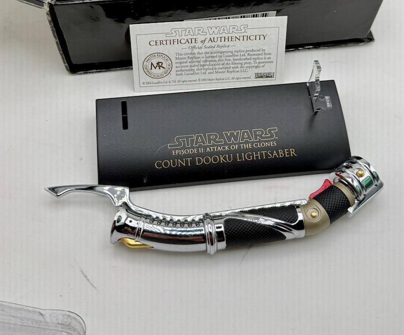 Puede incluir: Una r&eacute;plica del sable de luz del Conde Dooku de Star Wars: Episodio II - El Ataque de los Clones. El sable de luz tiene una empu&ntilde;adura plateada con detalles en negro y rojo. Incluye un certificado de autenticidad y un soporte de exhibici&oacute;n.