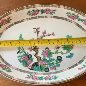 May include: A white oval serving platter with a green, pink, and black floral design. The platter measures 11 inches in length.