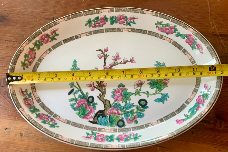 May include: A white oval serving platter with a green, pink, and black floral design. The platter measures 11 inches in length.