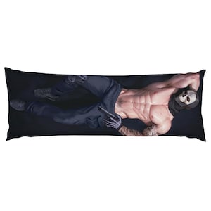 Puede incluir: Una funda de almohada rectangular con una ilustración de una figura musculosa con una máscara de calavera, sosteniendo una pistola. La figura lleva pantalones y guantes oscuros, con un tatuaje visible. El fondo es negro.