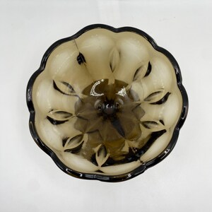 May include: A vintage brown glass bowl with a dark brown rim. The bowl has a scalloped edge and a textured, leaf-like pattern on the interior. The bowl is likely used for serving or display.