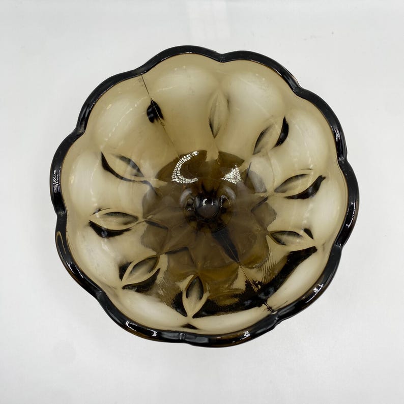 May include: A vintage brown glass bowl with a dark brown rim. The bowl has a scalloped edge and a textured, leaf-like pattern on the interior. The bowl is likely used for serving or display.