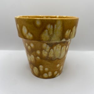 May include: A brown ceramic planter with a white marbled glaze. The planter has a rounded bottom and a wide opening.