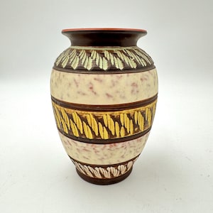 May include: A decorative ceramic vase with a brown base and rim, featuring bands of cream, brown, and yellow. The cream sections have a speckled pattern, while the brown and yellow bands have a textured, leaf-like design. The vase has a rounded shape.