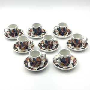 May include: Set of eight espresso cups and saucers. Each cup and saucer features a white background with a repeating pattern of abstract shapes in shades of brown, blue, and orange. The cups have small handles.