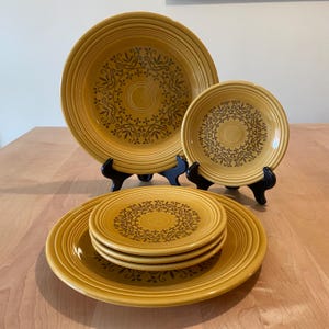 May include: Set of six yellow dinner plates with a brown floral pattern. The plates are stacked in two groups, one group of three and one group of two.