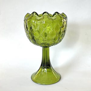 May include: A green glass pedestal bowl with a diamond pattern and a ruffled rim. The bowl sits on a slender stem and a flared base. The glass has a slight transparency.