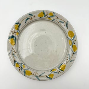 May include: A white ceramic plate with a yellow floral design around the rim. The flowers are yellow with green leaves and white dots.