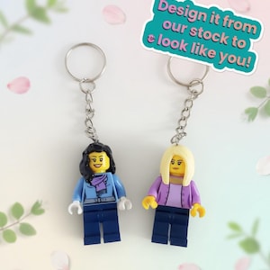 May include: Two Lego-style keychains featuring miniature figures with yellow heads, attached to silver keyrings. One figure wears a blue jacket and scarf, the other a purple jacket. Text on a teal background reads: "Design it from our stock to look like you!"