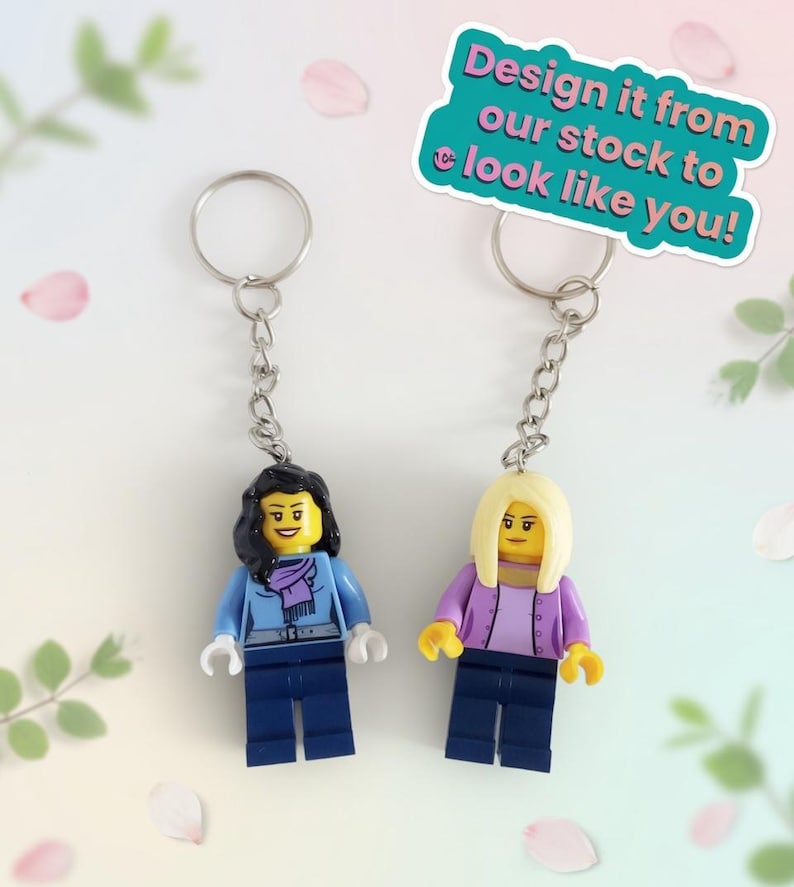 May include: Two Lego-style keychains featuring miniature figures with yellow heads, attached to silver keyrings. One figure wears a blue jacket and scarf, the other a purple jacket. Text on a teal background reads: "Design it from our stock to look like you!"