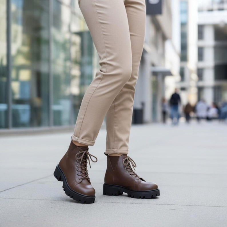 K&ouml;nnte beinhalten: Braune Schn&uuml;rstiefel aus Leder mit einer klobigen schwarzen Sohle. Die Stiefel haben eine runde Spitze und werden mit beigefarbenen Hosen getragen. Die Stiefel sind etwa 15 cm hoch.